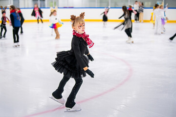 Little girl in reindeer costume skating on ice rink, children's sports festival.