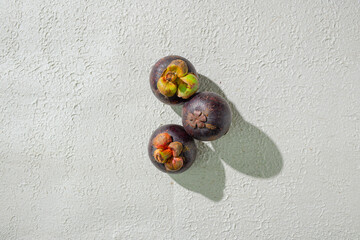 Mangosteen fruit displayed against a textured white background, emphasizing its unique purple rind and freshness