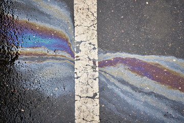 Gasoline or oil polluting wet asphalt road creating rainbow pattern next to a white dividing line