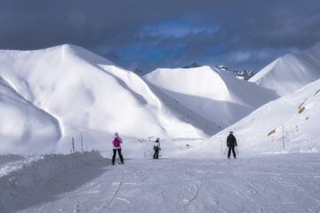 Skiers navigate stunning white slopes beneath majestic mountains and cloudy skies, creating a breathtaking winter scene that captivates adventure enthusiasts, Montgenevre ski village, Alps, France