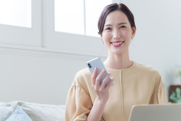 家でパソコンとスマホで仕事する女性