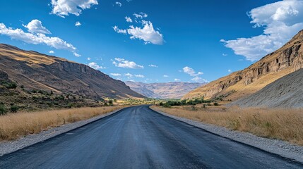 A serene road stretches through a mountainous landscape under a clear blue sky.