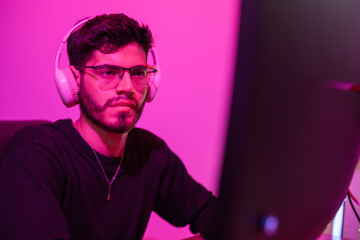 Obraz premium Young man engaged in gaming with headphones in a room illuminated by pink light