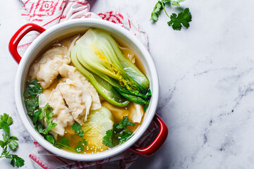 Gyoza soup with mushroom broth and bok choy in red saucepan. Asian cuisine concept.