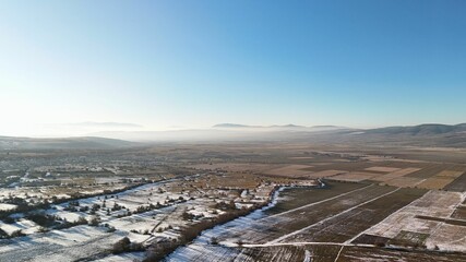 Aerial view of winter landscape with fields and mountains.