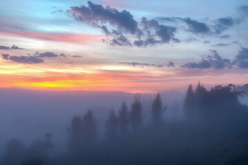 Misty autumn sunny sunrise in mountains. rural scenery with colorful sky light. countryside landscape rolling in to the distant valley full of fog