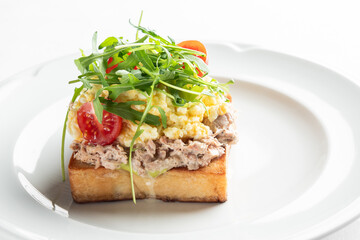 A delicious open-faced sandwich with a toasted slice of bread topped with creamy tuna salad, fresh cherry tomatoes, and a sprinkle of arugula. Perfect for a light meal or snack.