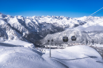 Snowcovered mountains and a clear blue sky create a stunning scene. A gondola glides above, inviting outdoor enthusiasts to explore, Montgenevre ski village, Alps, France