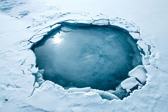 Melting ice creating a deep blue water pool surrounded by thick snow and ice on a frozen lake during winter, creating a beautiful contrast between the cold white snow and the deep blue water - Powered by Adobe