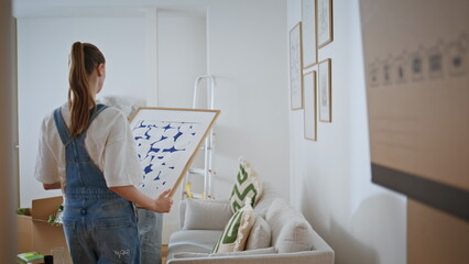 Cheerful couple discussing decor new apartment. Married pair arranging artworks