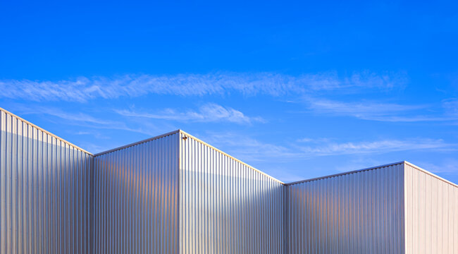 Factory warehouse industry building with geometric metal corrugated steel wall and rooftop against blue sky background, Modern industrial exterior architecture backdrop design in minimal style