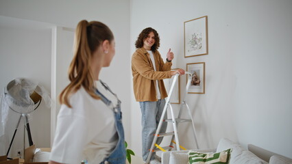 Happy couple arranging apartment decoration in light living room. Smiling woman