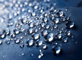 Close-up view of numerous water droplets on a dark surface.  The droplets vary in size and exhibit high reflectivity, creating a glistening effect.  The background is a deep, blurry blue.