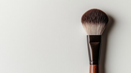 A soft-bristle makeup brush, positioned diagonally on a clean white surface,