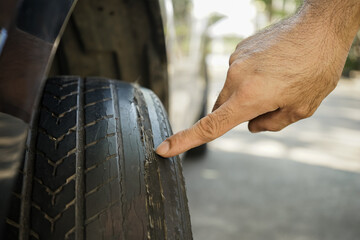 close up of hand points at a worn tire with bald tread. Concept of car maintenance and dangers from...