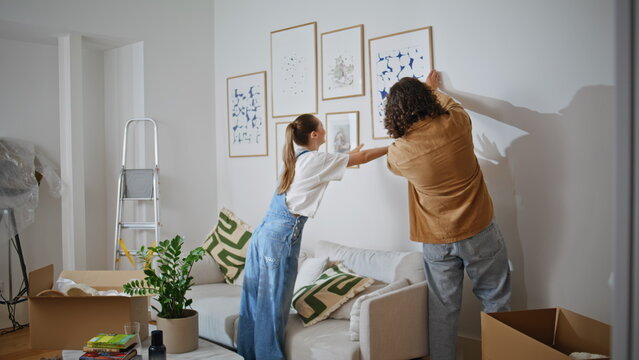 Couple hanging pictures wall apartment. Happy woman and man enjoy collaborating 