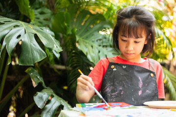 Asian young girl painting at an easel, in creativity and artistic expression, against natural backdrop. It highlights outdoor painting, art education, and the joy for promoting child creativity.