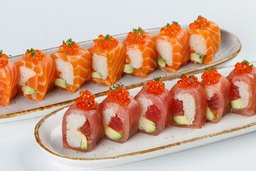 Ceramic tray with variety of salmon  end tuna sushi roll with avocado, appetizing japanese meal.