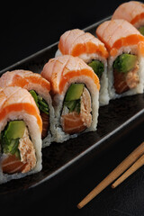 Close-up of salmon sushi rolls on a black plate with chopsticks
