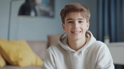 Joyful teenage boy smiling and gesturing while recording video at home in cozy interior with soft blue and beige tones for modern vlog content creation