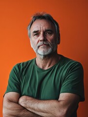 Obraz premium Middle-aged man with gray beard wearing green shirt poses confidently against vibrant orange background showcasing ample copyspace for text.