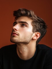 Obraz premium Modern Young Man in Thoughtful Pose Against Warm Brown Studio Background with Abundant Copy Space for Text and Bright Color Accents