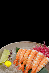 Shrimp sashimi with lime and ice on a bamboo leaf on a black background