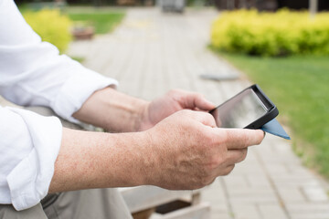 Close-up of senior male hands holding a tablet outdoors. The image highlights themes of technology, connectivity, active aging, and modern lifestyle in a natural setting
