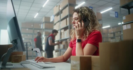 Female customer support specialist in logistics talks to customer on mobile phone, uses computer, works in postal service or online store storage. Sorting center workers carrying cardboard boxes.
