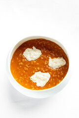 A white bowl filled with creamy orange soup, topped with dollops of sour cream. The dish is elegantly presented against a neutral background, highlighting its rich texture and color.