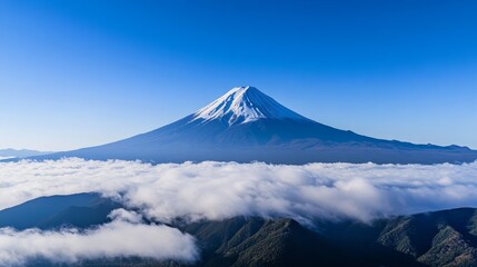 A majestic view of Mount Fuji rising above the clouds, framed by a clear blue sky, showcasing its snowy peak and lush green foothills.