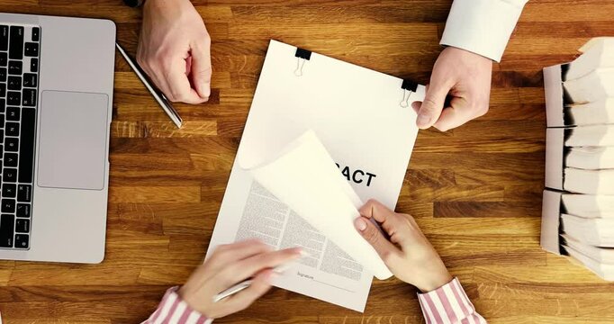 A business meeting scene is showcasing crucial document exchange over a polished wooden table with a laptop setup