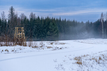 Hunting Platform in Snowy Field Near Forest. Winter Landscape with Mist and Wooden Hunting Tower.
