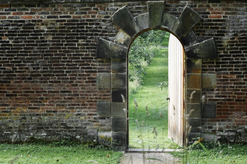 English wall garden entrance. Invitation to the spring concept. Half opened door into the beautiful summer orchard