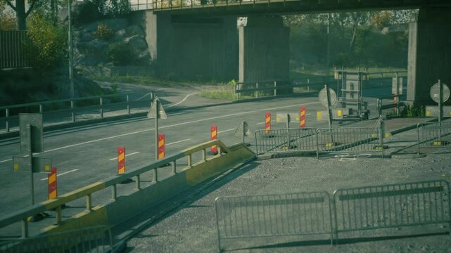 Barriers and warning signs surround a construction site along a busy urban roadway. Trucks and vehicles navigate around the restrictions in the area during daylight.