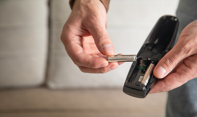Man installs a new battery in the remote control of a TV.