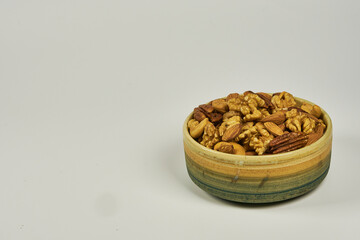 Assorted nuts in a stoneware container with a straw basket, on a white background. Almonds, Walnuts, Cashews and Chestnuts