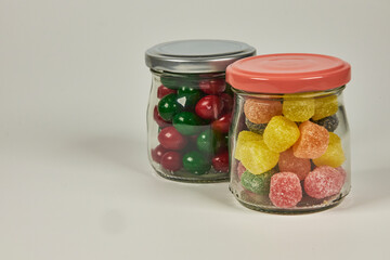 Jelly candies and dipped chocolates, in various bright and vivid colours, in suitable containers, on a white background.