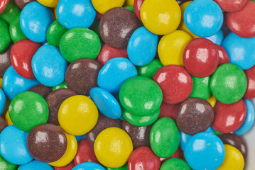Chocolate dragees, covered with caramel of different colors, in a container on a white background
