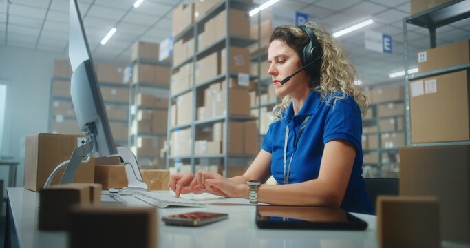 Female logistics coordinator wearing headset chats with customer on call, uses computer, works in post office or E-commerce store storage. Sorting center workers carrying cardboard boxes for delivery.
