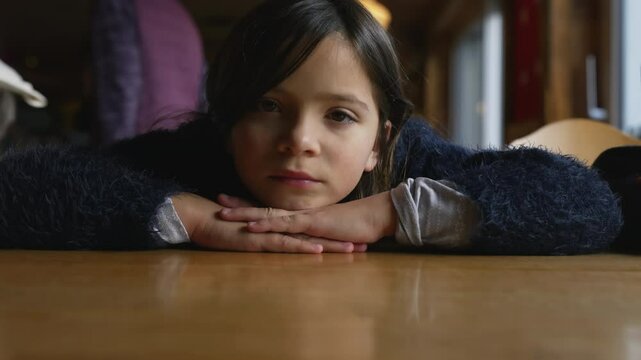 Sad thoughtful little girl feeling down while leaning on restaurant table, closeup of pensive depressed 8 year old child