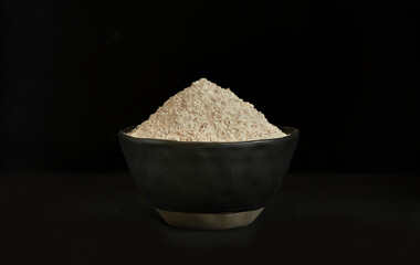Macrophotography of whole grain flour in dark ceramic bowl on dark background