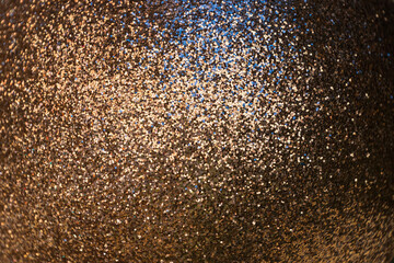 A close-up view of a shimmering golden surface, densely packed with fine glitter particles,...