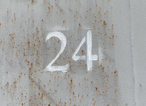 White number 24 on aged gray background. Twenty four on textured rusty surface 