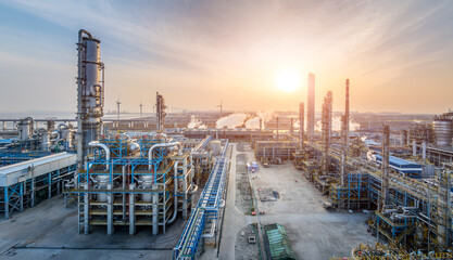 Large industrial oil refinery plant at sunset with multiple pipelines and smokestacks.