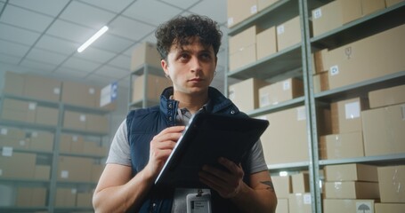 Male logistics specialist uses tablet computer and digital pencil, checks inventory. Warehouse...