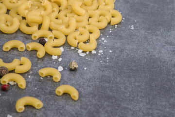 Raw macaroni pasta with sea salt and pepper on grey background