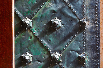 Weathered metal surface with a diamond pattern, featuring rivets and raised hexagonal bolts at...