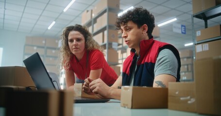 Two warehouse workers or logistics specialists scan parcel with scanner, prepare order for shipping to client, check information on laptop computer, work in post office. Online store delivery service.