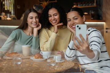Women taking selfie at coffee meeting in cafe, view through window
